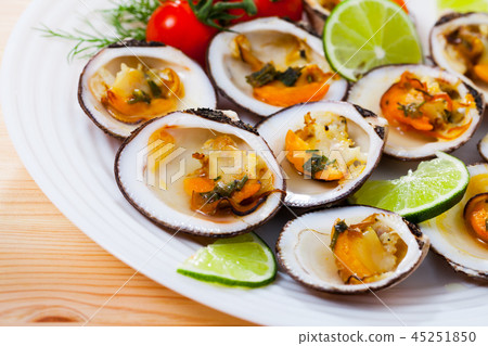 Tasty dog cockle baked in oven with sauce, served with lemon and greens 45251850