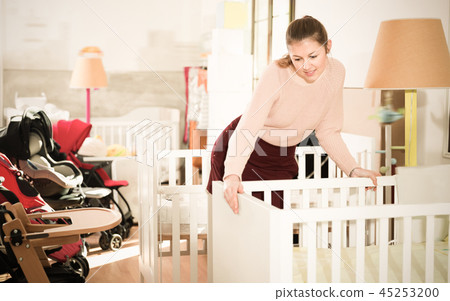 Girl buyer choosing wooden crib in the shop of furniture for bab Girl buyer choosing wooden crib in the shop of furniture for bab 45253200