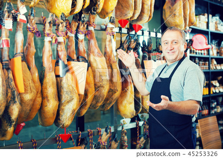 Positive mature man seller with jamon in local market Positive mature man seller with jamon in local market 45253326
