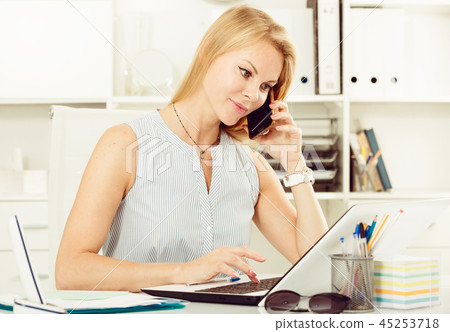 Portrait of blond adult girl in office talk on telephone 45253718