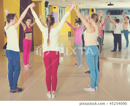 Teenage boys and girls practicing circle dance with female trainer in dance hall 45254090