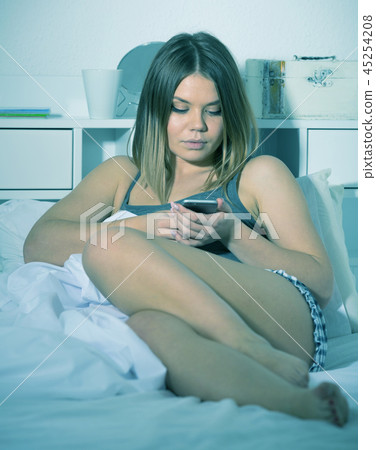 Smiling girl lying and using smartphone on bed in bedroom 45254208