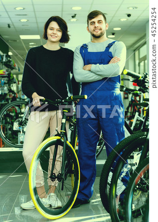 Young woman and seller standing with bicycle in the store indoor Young woman and seller standing with bicycle in the store indoor 45254254