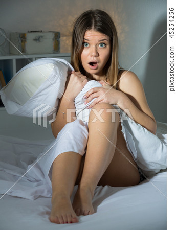Worried young woman is oversleep, sitting on bed in bedroom Worried young woman is oversleep, sitting on bed in bedroom 45254256