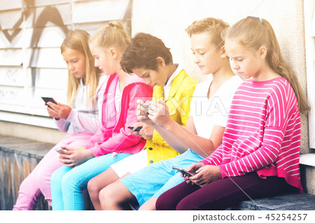 Cheerful children are chatting on their smartphone Cheerful children are chatting on their smartphone 45254257