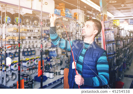 interested male choosing fishing rod for fishing in the sports shop interested male choosing fishing rod for fishing in the sports shop 45254538