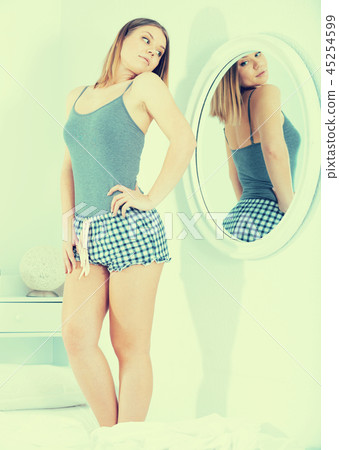 Young female in pygama, using mirror in bedroom Young female in pygama, using mirror in bedroom 45254599