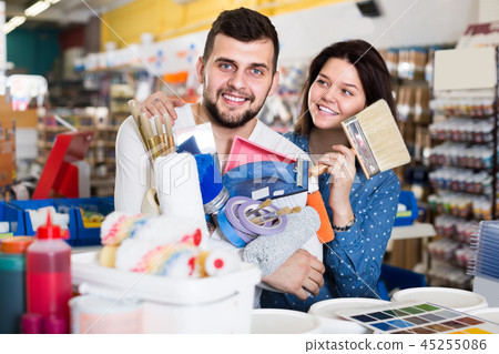 Young active couple demonstrating tools for house renovating in paint store 45255086