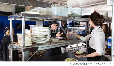 Woman waiter is giving order to chef cook on kitchen in restaurant. 45255487