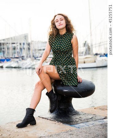 Young attractive woman tourist sitting at stone in port with sailboats Young attractive woman tourist sitting at stone in port with sailboats 45255751