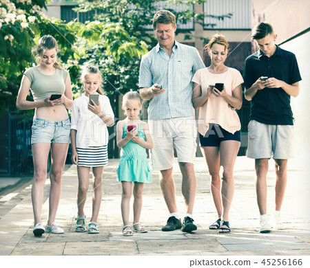 Portrait of large family standing with their mobile phones together outdoors Portrait of large family standing with their mobile phones together outdoors 45256166