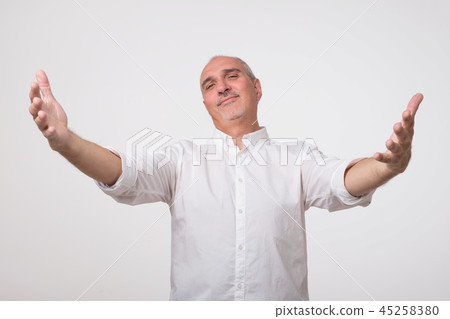 You are welcome concept. Cheerful mature man in white shirt gesturing welcome sign and smiling 45258380
