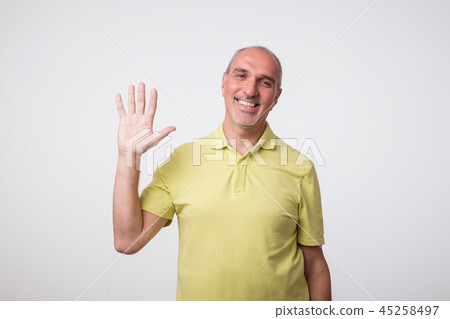 Friendly-looking attractive european man waives hand in hello gesture while smiling cheerfully. 45258497