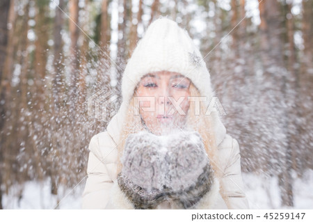Christmas, holidays and season concept - Young happy blond woman blowing snow in the winter nature 45259147