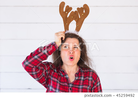 Christmas, holidays and people concept - a woman's head with deer horns on it. Woman scratches her Christmas, holidays and people concept - a woman's head with deer horns on it. Woman scratches her 45259492