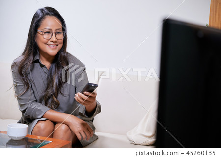 Smiling ethnic woman using TV Smiling ethnic woman using TV 45260135