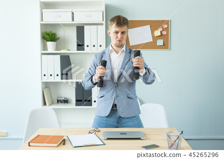 Business, fitness in office and people concept - handsome man in office holding dumbbell in hand Business, fitness in office and people concept - handsome man in office holding dumbbell in hand 45265296