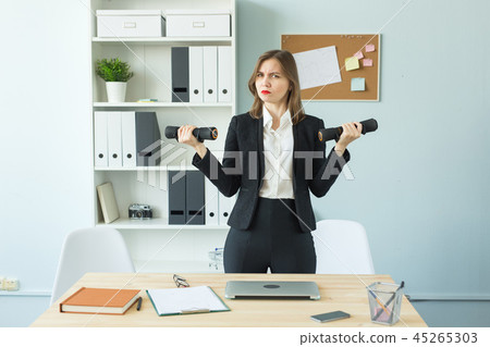 Business, emotions and people concept - Woman in office holding dumbbell's in hands Business, emotions and people concept - Woman in office holding dumbbell's in hands 45265303