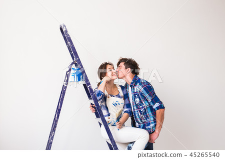 People, renovation and repair concept - young couple doing a redecoration and kissing in new People, renovation and repair concept - young couple doing a redecoration and kissing in new 45265540