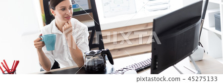 A young girl sitting at a table in the office and holding a Cup. A young girl sitting at a table in the office and holding a Cup. 45275133