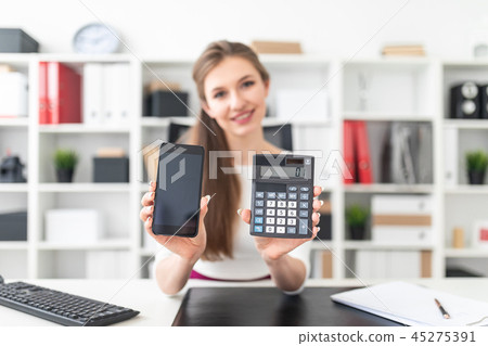 A young girl sitting at a table and holding a phone and a calculator. A young girl sitting at a table and holding a phone and a calculator. 45275391