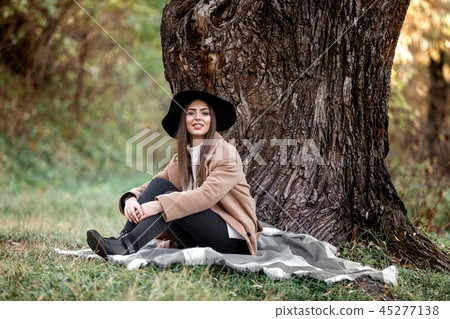 beautiful woman in black hat sitting under big tree 45277138