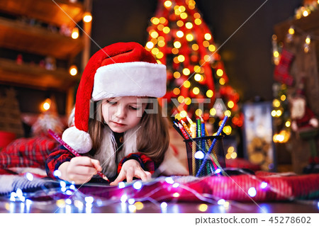 Funny girl in Santa hat writes letter to Santa Funny girl in Santa hat writes letter to Santa 45278602