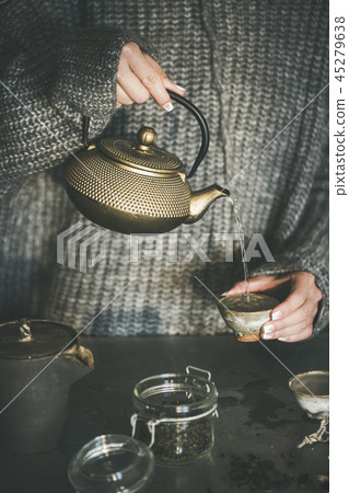 Female in sweater pouring green tea from pot into cup 45279638
