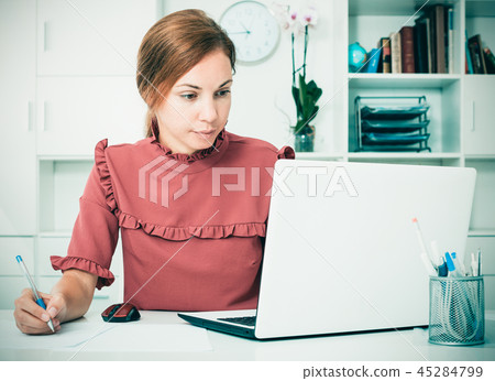 Woman working with laptop and taking notes 45284799