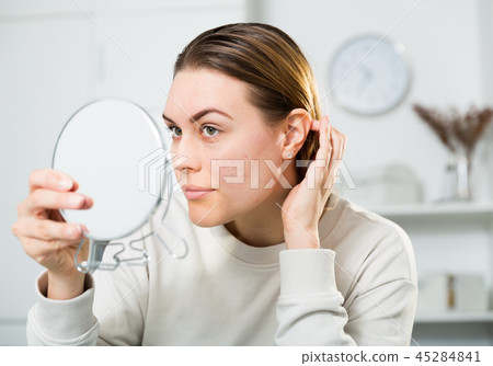 Cheerful woman is concentrared looking on her face in the mirror 45284841