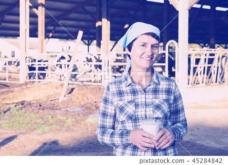 Confident female milker approvingly demonstrating milk on dairy farm 45284842