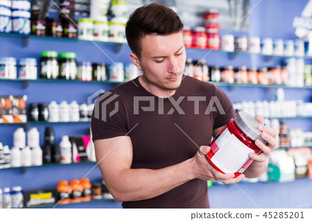 Young muscular man choosing sport nutrition products in shop 45285201