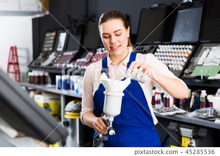 Girl in workwear pouring paints in spraying gun Girl in workwear pouring paints in spraying gun 45285536