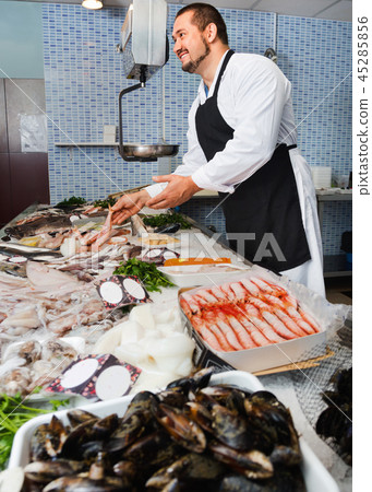 Seller in black apron shows fish counter 45285856