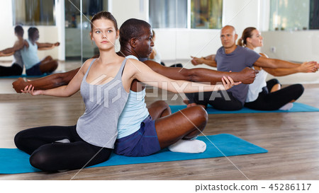 Women and men exercising in pairs during yoga class in modern fitness center Women and men exercising in pairs during yoga class in modern fitness center 45286117