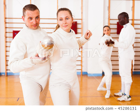 Girl fencer exercising new techniques with trainer indoors Girl fencer exercising new techniques with trainer indoors 45286131