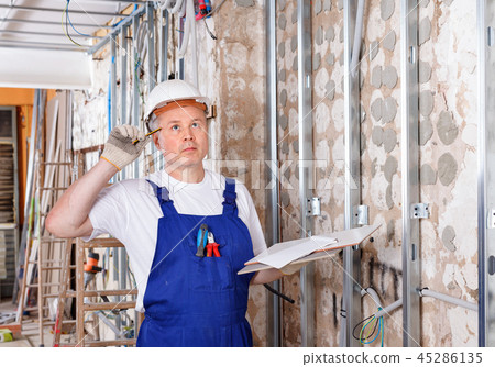 Focused construction worker inspecting room and planning upcoming repairs Focused construction worker inspecting room and planning upcoming repairs 45286135