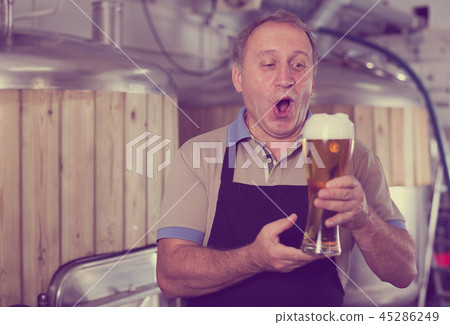 Brewer is standing with beer with foam in glass on his workplace Brewer is standing with beer with foam in glass on his workplace 45286249