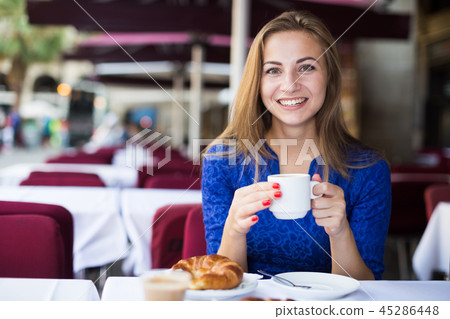 Young woman is lunching with croissant and coffee Young woman is lunching with croissant and coffee 45286448