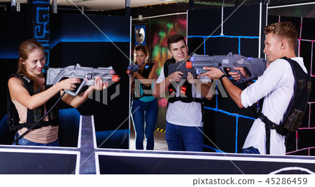 Laser tag players guys and girls playing in teams in dark laser tag room Laser tag players guys and girls playing in teams in dark laser tag room 45286459