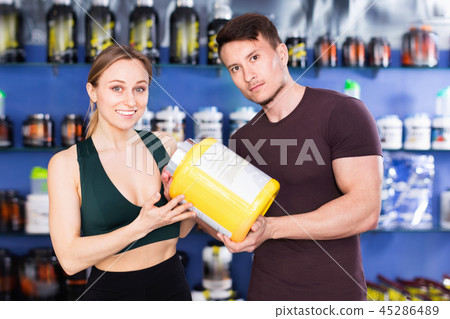 Happy young sporty people standing in store, holding big can of sport nutrition Happy young sporty people standing in store, holding big can of sport nutrition 45286489