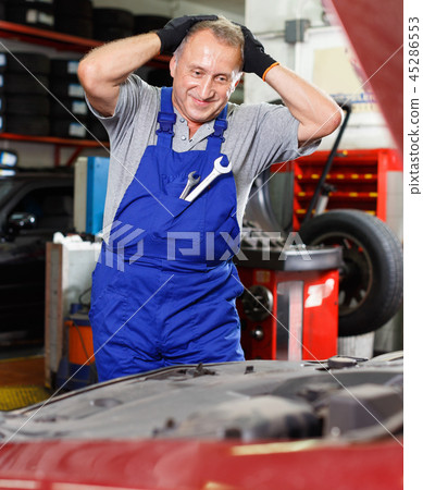 Puzzled male mechanic inspecting broken car and determining scope of work at auto service 45286553