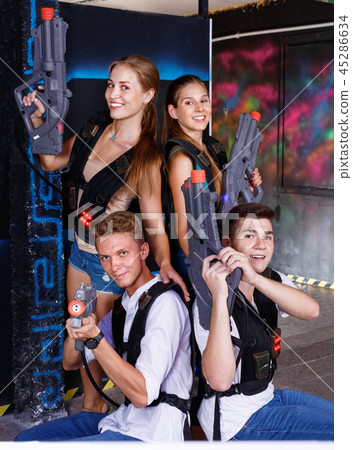 Group portrait of joyful young people with laser guns in their hands in room for playing laser tag Group portrait of joyful young people with laser guns in their hands in room for playing laser tag 45286634