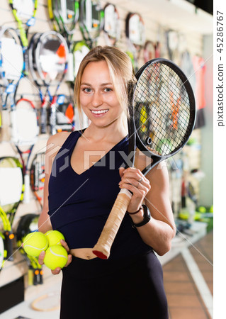 Female standing in sporting goods store with balls and racket 45286767