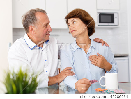 Unhappy mature couple sittimg at kitchen table and taking drugs in home 45286984