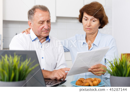 Mature man and woman with documents talking while working at laptop Mature man and woman with documents talking while working at laptop 45287144