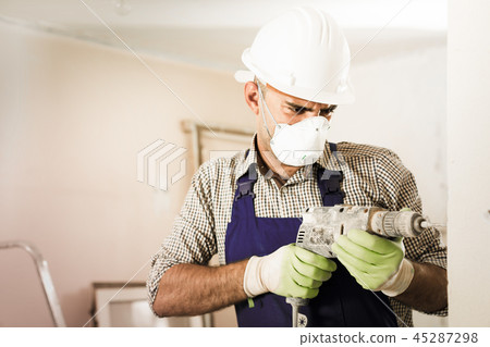 Portrait of repairer man standing with drill indoors Portrait of repairer man standing with drill indoors 45287298