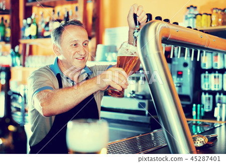 Barman is pouring unbottled beer with foam for client in the bar. Barman is pouring unbottled beer with foam for client in the bar. 45287401