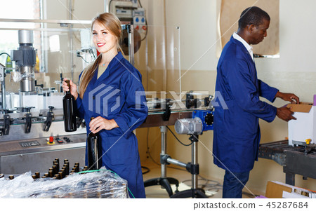 Two cheerful winery workers checking bottles with wine before packing Two cheerful winery workers checking bottles with wine before packing 45287684