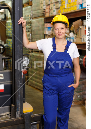 Young female worker in uniform and helmet with car standing in build store 45287745